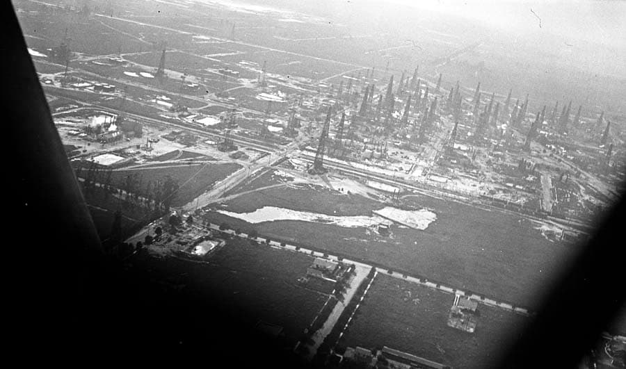 An aerial view of a massive, densely packed oil field filled with dozens of tall wooden oil derricks.