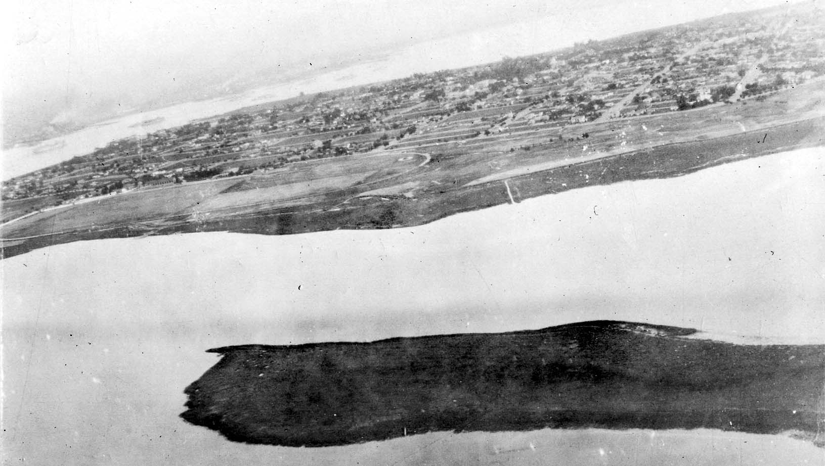 An aerial photograph showing a long coastal peninsula or island stretching across the water, heavily developed with roads and housing.