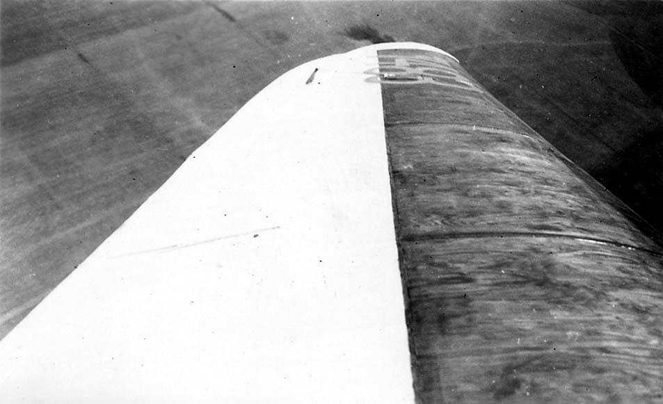 An aerial view from an aircraft cockpit looking past the fabric-covered leading edge and wingtip over a flat Southern California landscape.