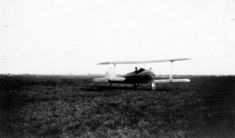 A single-engine biplane parked quietly in the middle of a vast, open grassy field.