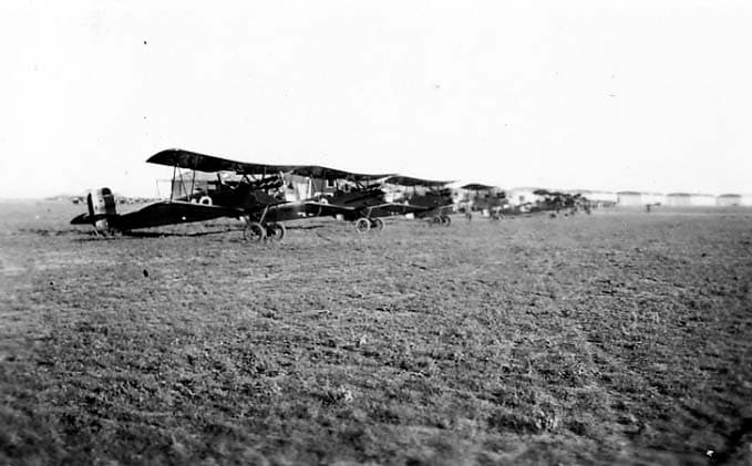 A long line of dark-colored Army Air Corps training biplanes parked on the grassy airfield.