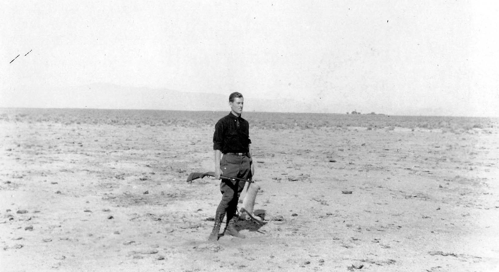 Donald A. Hall Sr. standing in a vast, barren desert landscape holding a rifle.