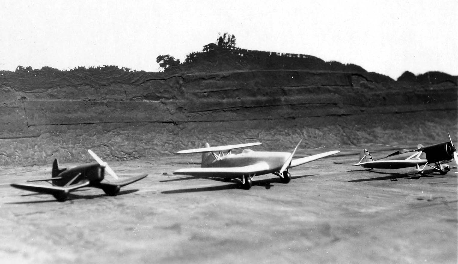 A low-angle photograph of three experimental aircraft wind tunnel models lined up on a factory roof with distant hills in the background.