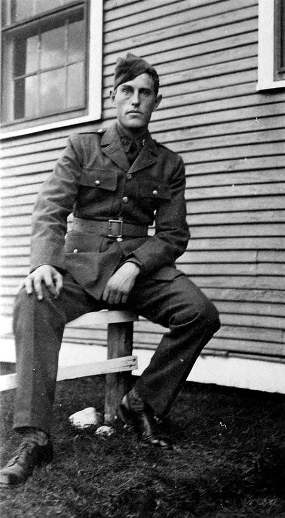 A portrait of a young Army Air Corps flight cadet in full uniform sitting on a wooden bench outside a barracks building.