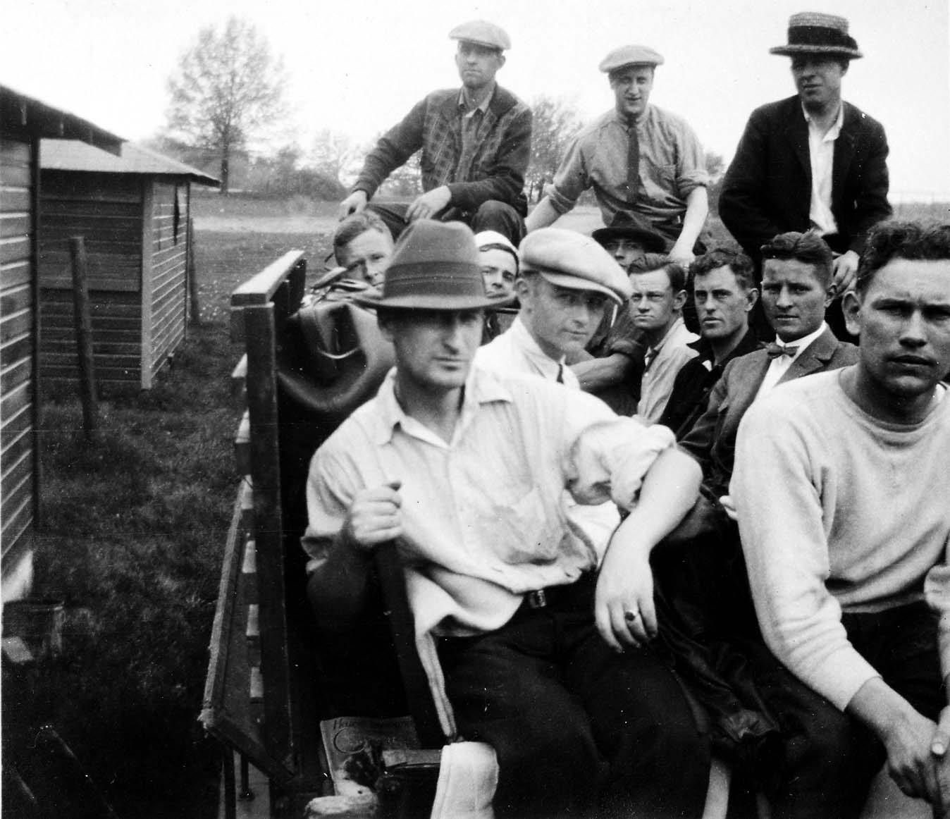 A large group of young men, some in civilian clothes and flat caps, crowded together in the back of an open transport truck.
