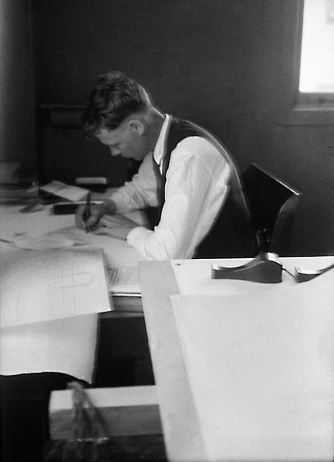 Charles Lindbergh sitting at a drafting table, writing intently on original navigational charts for the transatlantic flight.