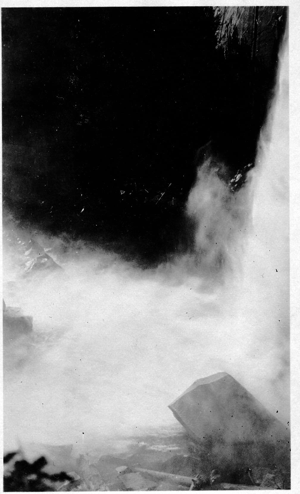 Heavy clouds of white water spray and mist rising from the roaring base of Nevada Fall around a massive granite boulder.
