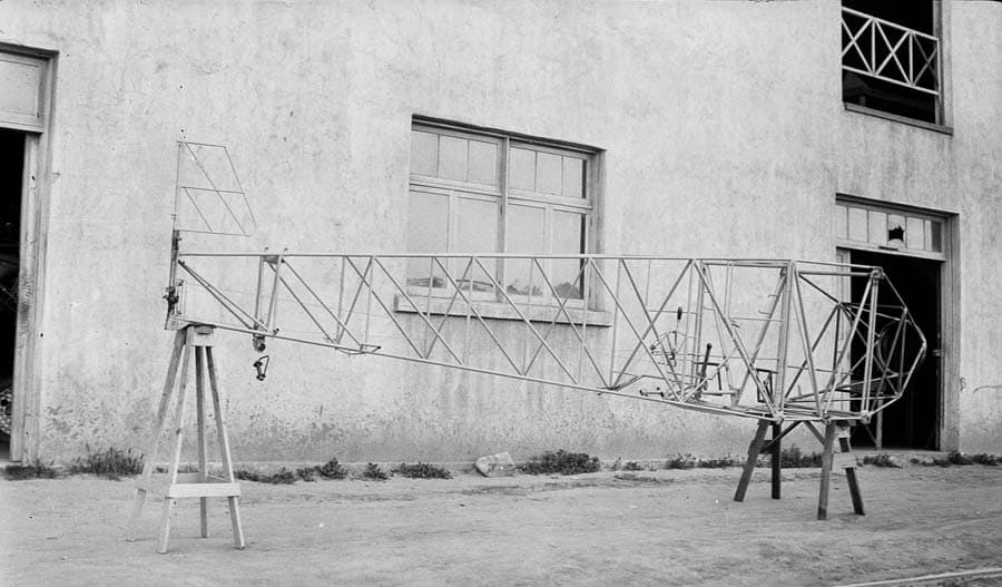 The raw, completed tubular steel fuselage framework of the Spirit of St. Louis resting on wooden sawhorses outside the Ryan Airlines factory building.