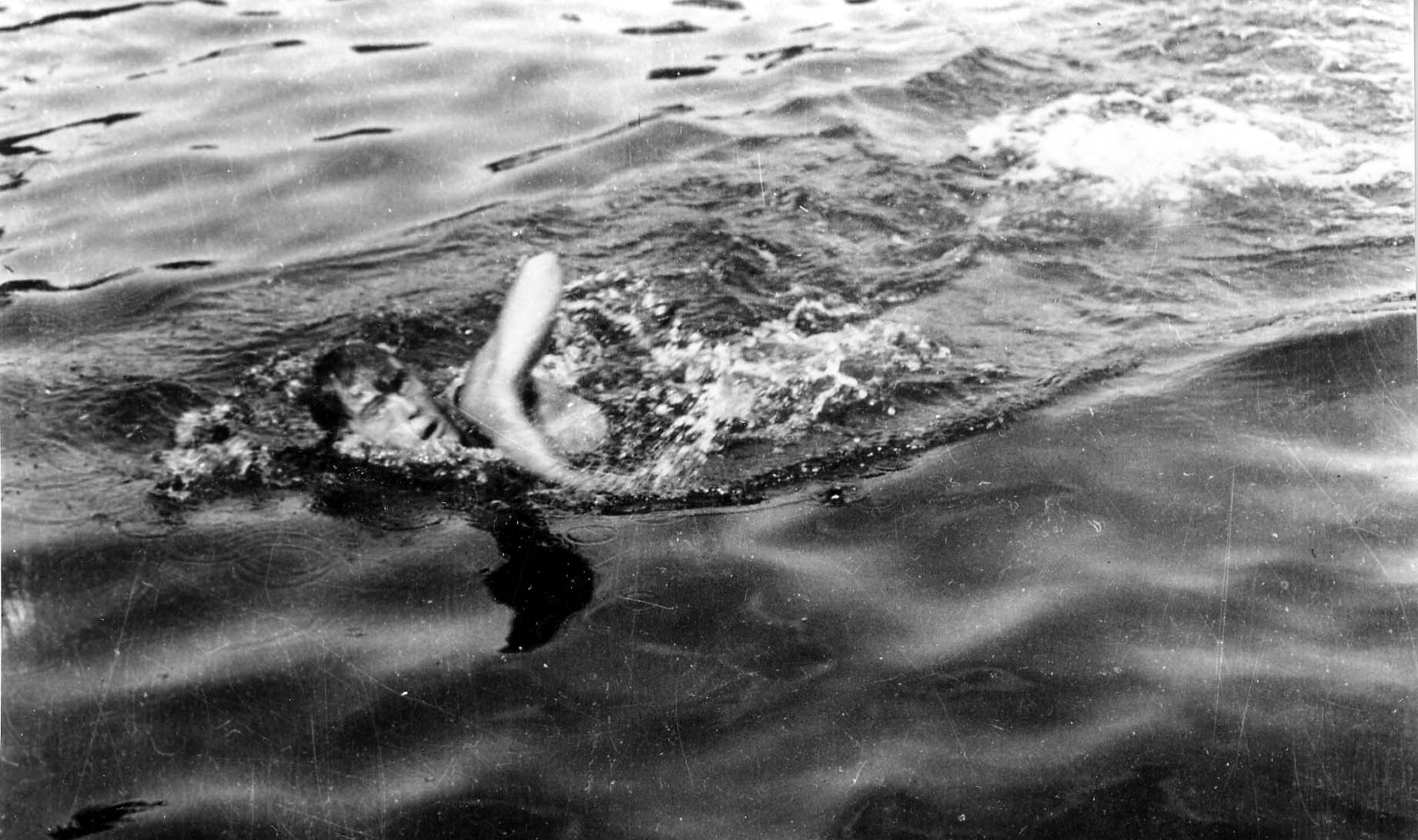 A close-up action shot of a Donald A Hall taking a breath mid-stroke in dark open water.