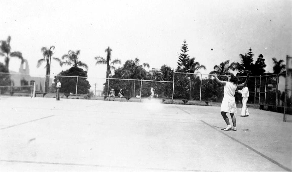 A woman preparing to serve a tennis ball during an outdoor mixed doubles match.