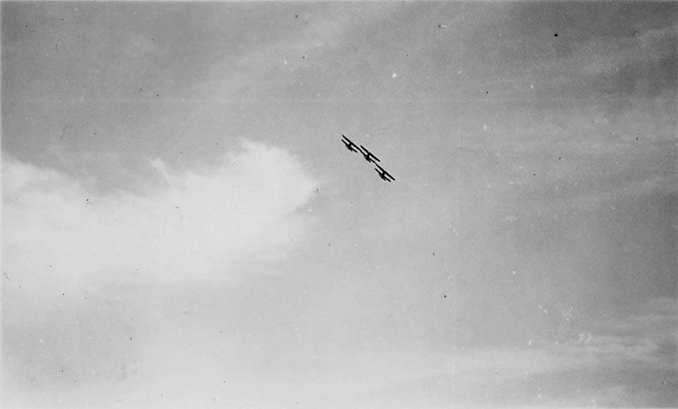 A distant view of three biplanes executing a steep, coordinated climb against a cloudy sky.
