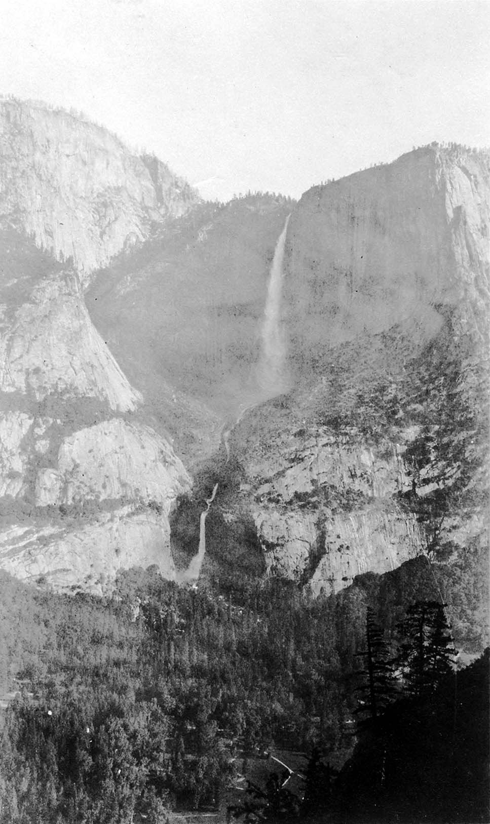 A distant high-altitude view across Yosemite Valley capturing Upper and Lower Yosemite Falls plunging down towering north wall cliffs.