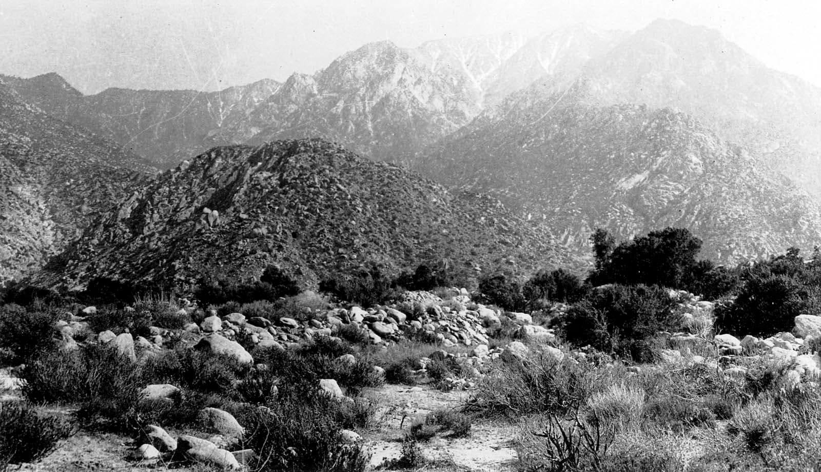 An expansive view of rolling mountain foothills covered in sparse desert brush under a bright, hazy sky.