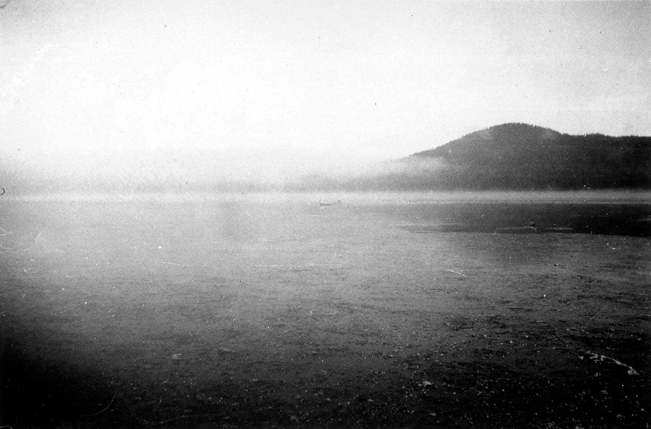 A moody, atmospheric view of Lake Cuyamaca blanketed in early morning mist and low-hanging fog over the water.
