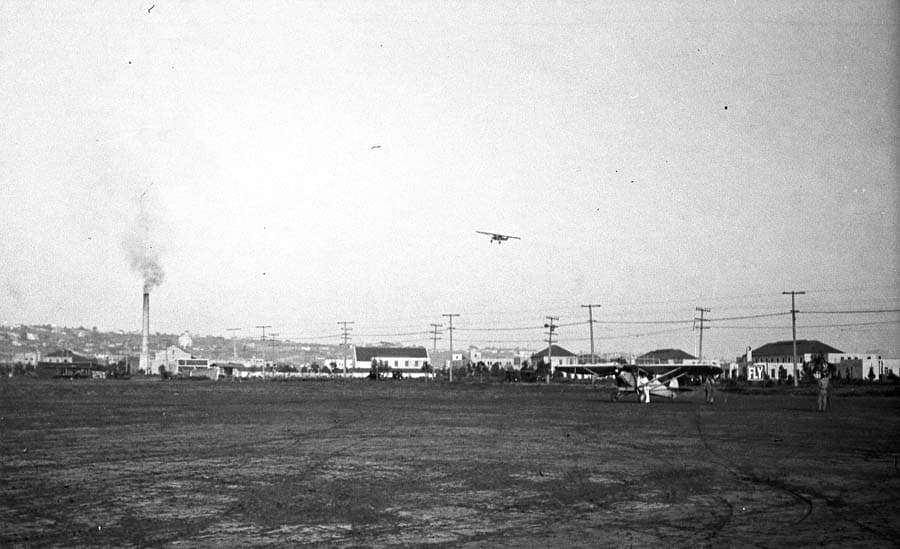 Airfield overview showing parked aircraft on flightline and the Spirit of St. Louis flying high overhead.