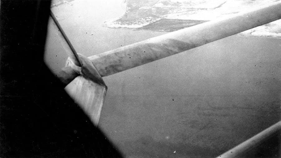 Aerial view from cockpit window looking along the streamlined wing strut down at the San Diego coastline and water.