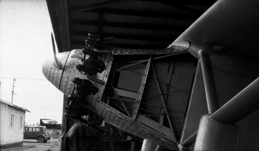Close-up under hangar roof of the uncowled Wright Whirlwind engine, fuselage mount, and propeller.