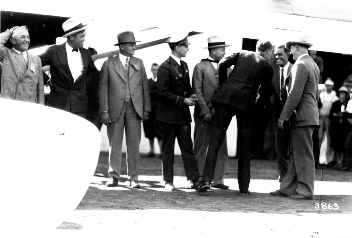 Archival photograph plate 3863 showing Charles Lindbergh greeting naval officers and civic leaders beneath an airplane wing.