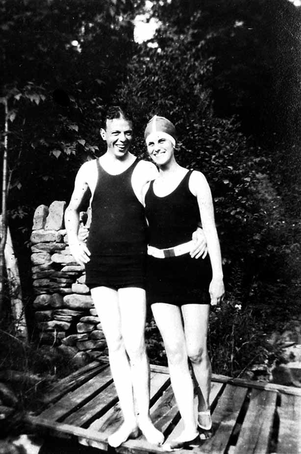 Donald A. Hall Sr.'s sister Alice Hall Smith and a companion in vintage black tank swimsuits smiling arm-in-arm on a wooden dock.