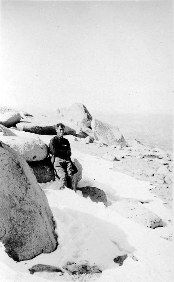 Donald A. Hall Sr. smiling while resting against granite boulders in a high-altitude mountain snowfield.