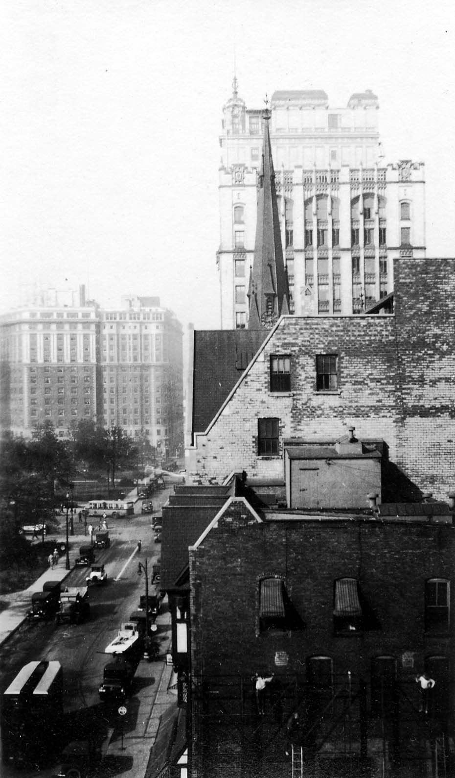 A high-angle telephoto view across brick rooftops capturing the Gothic spire of Central Methodist Church and the ornate Kales Building.