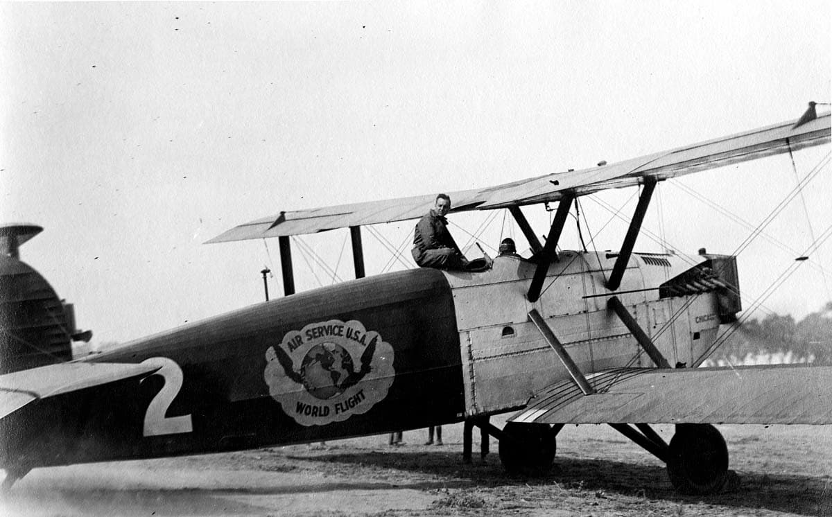Douglas World Cruiser No. 2 Chicago on wheeled landing gear with pilot seated on fuselage at an airfield flight line.