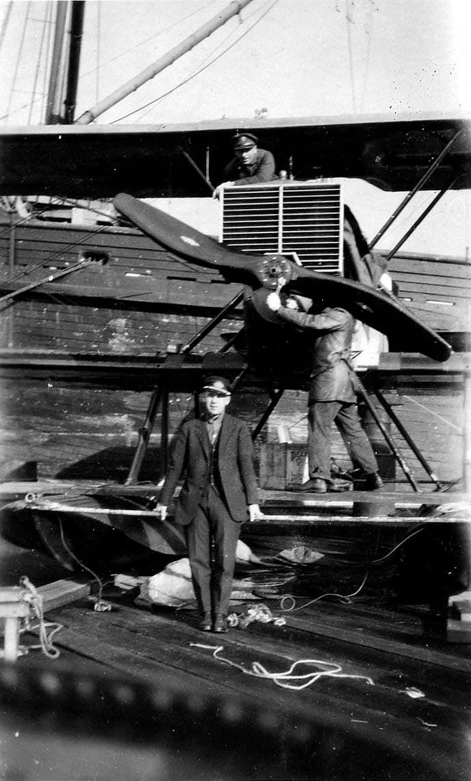 Mechanics adjusting the wooden propeller of a Douglas World Cruiser seaplane with an officer standing on the pontoon in the foreground.