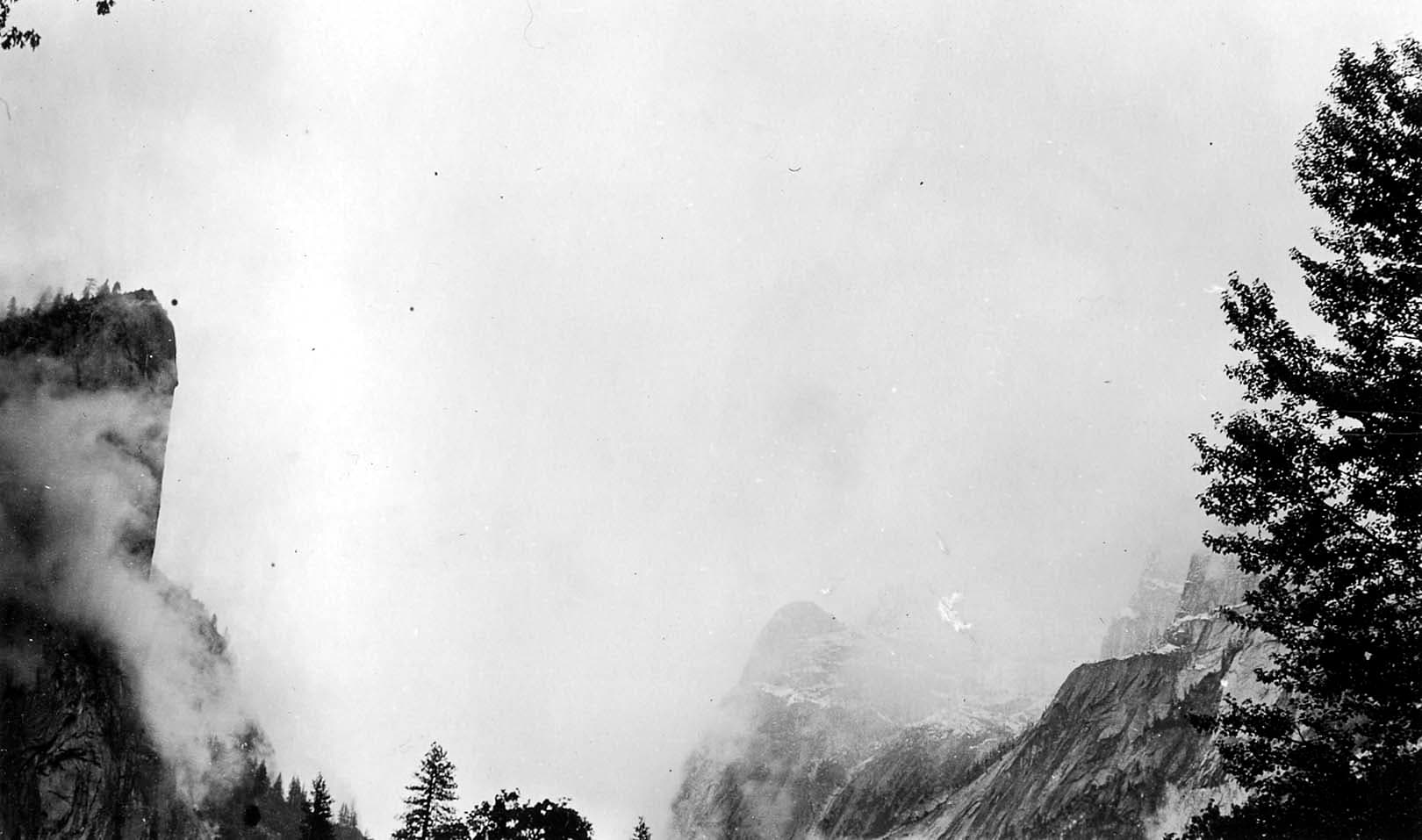 The sheer vertical cliff face of El Capitan emerging from low-hanging storm clouds and drifting winter mist in Yosemite Valley.