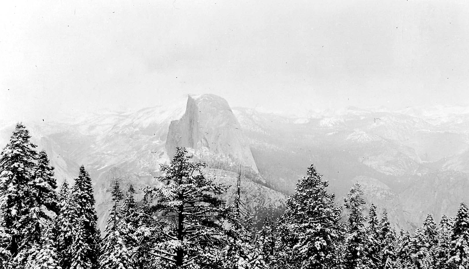 A sweeping panoramic winter view of Half Dome and the High Sierra peaks heavily blanketed in deep snow from Glacier Point.