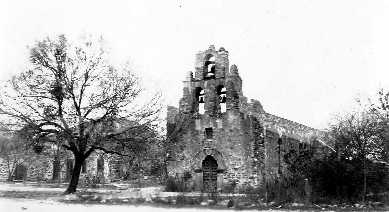 The historic stone facade of Mission San Francisco de la Espada in San Antonio showing its three-bell espadana and faceted arch portal.