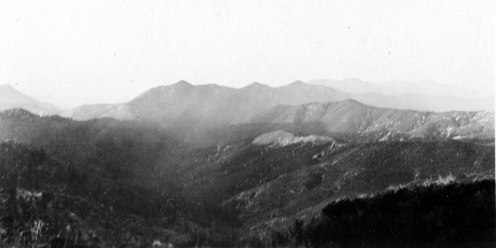 Distant mountain ranges with rolling crests fading into an atmospheric haze beneath a bright, washed-out sky.