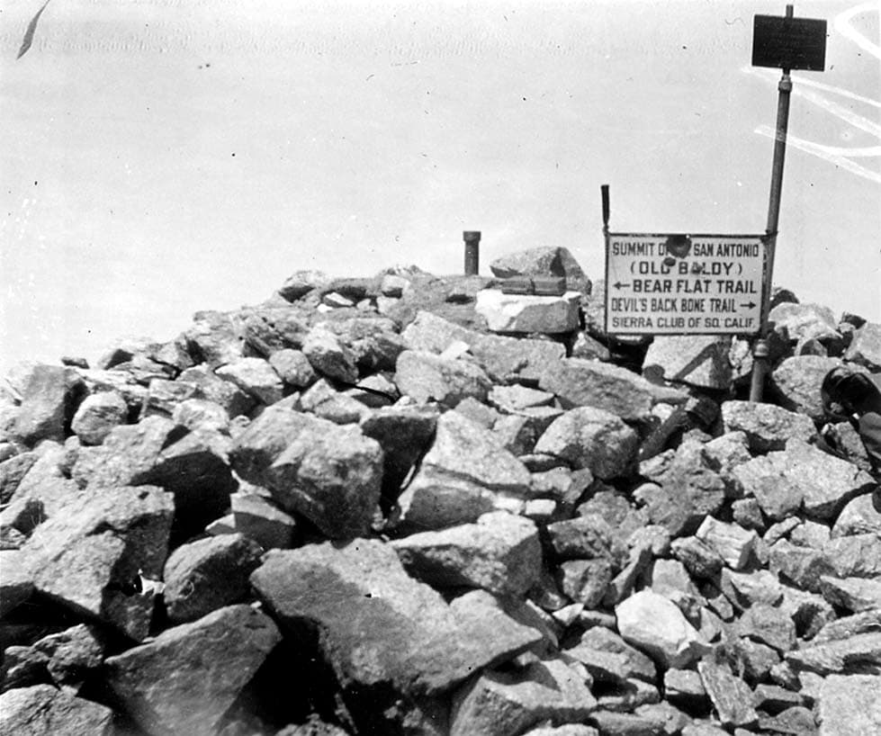 A historic Sierra Club wooden trail sign marking the summit of Mount San Antonio (Old Baldy) via Devil's Backbone and Bear Flat trails, perched atop a rocky summit cairn.