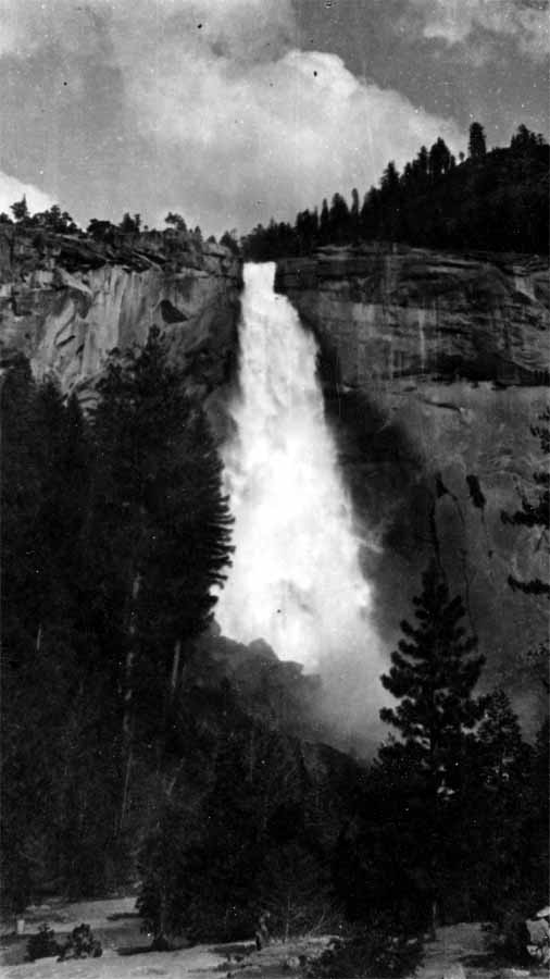 The full vertical plunge of Nevada Fall dropping over a steep granite cliff into misty evergreen woods along the Merced River.