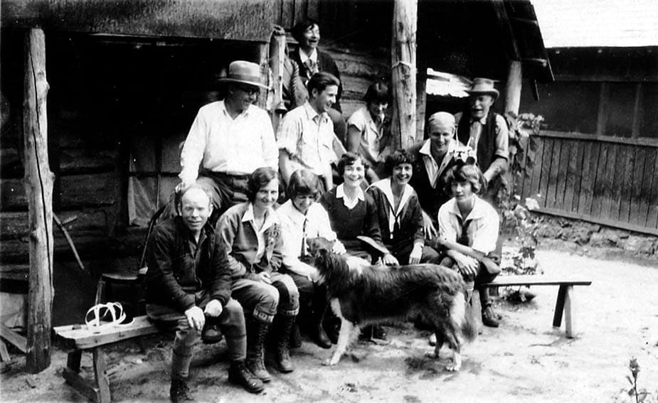 A group of male and female friends standing and sitting on a wooden bench at the camp.