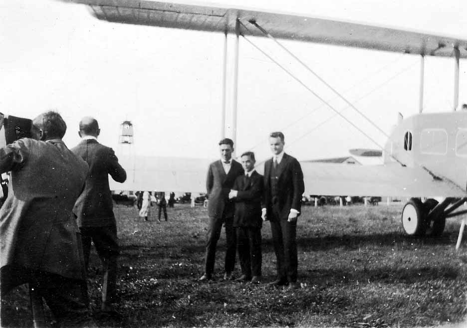 A press photographer with a large-format camera taking a picture of three men in suits standing before the Remington-Burnelli RB-2 lifting-body airliner.