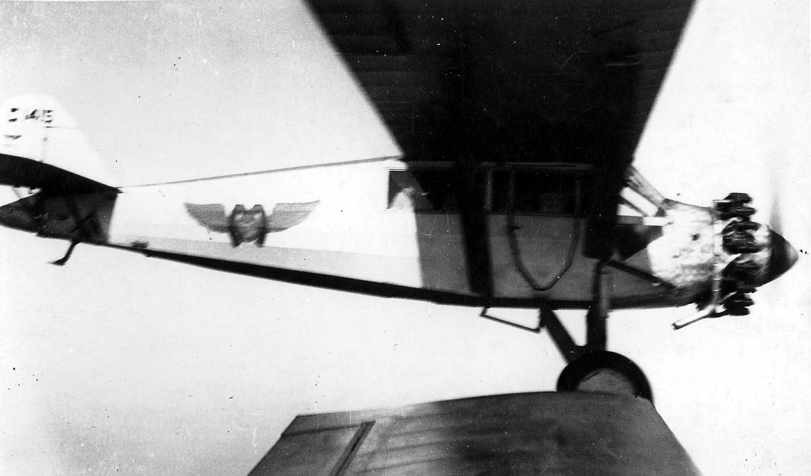 A close-up air-to-air profile of a Ryan B-1 Brougham cabin monoplane with Wright Whirlwind engine and winged fuselage logo in flight.