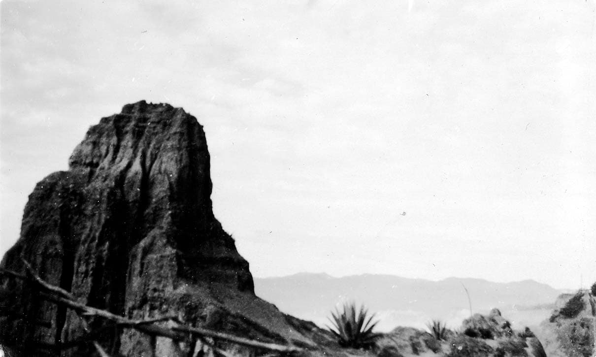 A massive eroded sandstone pinnacle rising dramatically along the cliffside of the Santa Monica Palisades, with agave plants and distant mountains.