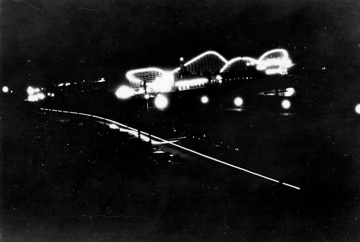 A night long-exposure photograph showing the illuminated outlines and undulating tracks of the wooden roller coaster on the Santa Monica Pier.