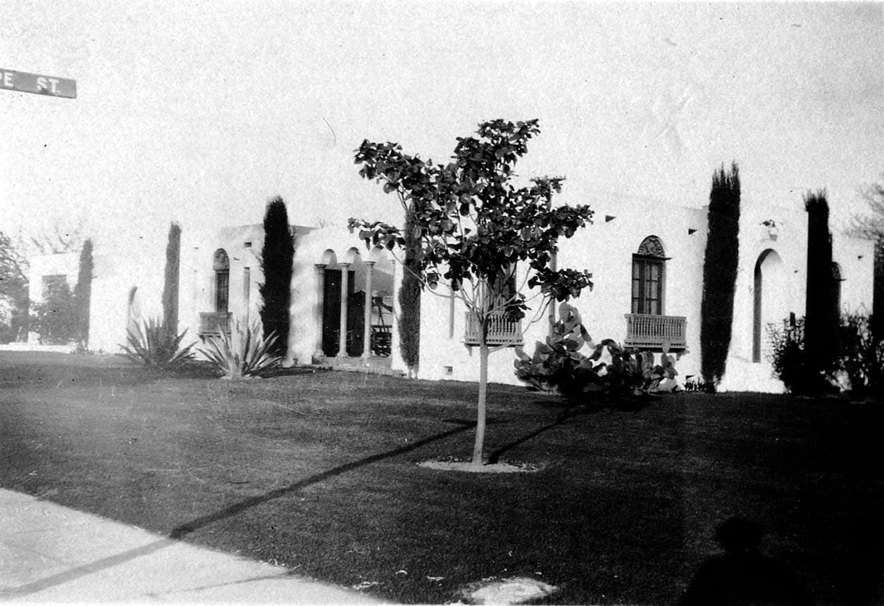 A sprawling Spanish Colonial Revival residential estate in Southern California featuring white stucco walls, arched loggia, and columnar cypress trees.