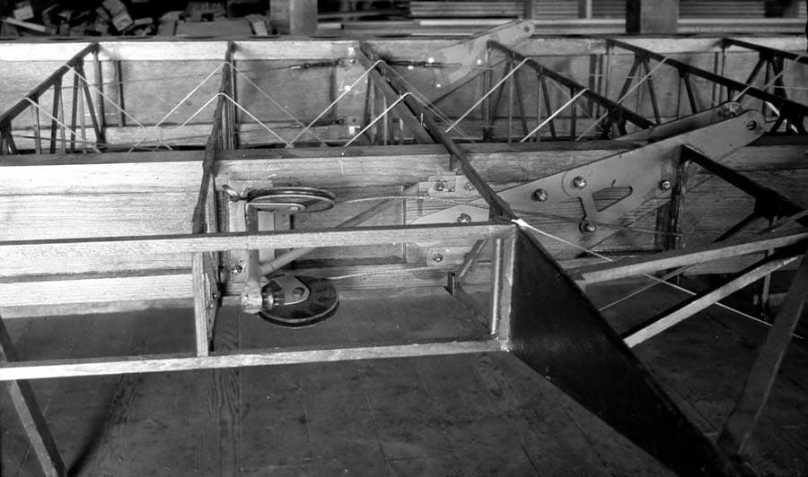 A detailed close-up of the exposed wooden wing ribs and the mechanical pulley and wire system used to control the aircraft's ailerons.