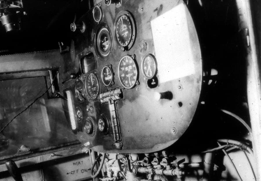 Interior photograph of the Spirit of St. Louis cockpit showing the instrument panel, periscope control, and fuel valve manifold.