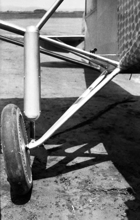 A front-angle view of the Spirit of St. Louis landing gear resting on the dirt at Dutch Flats, highlighting the aerodynamic shock cover.
