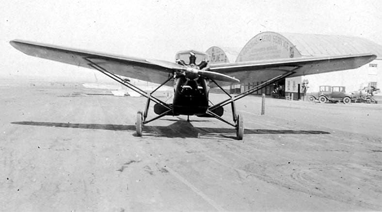Frontal view of a 1927 Stinson SM-1 Detroiter cabin monoplane on the tarmac at Long Beach Airport outside Arbogast Aero Service hangars.