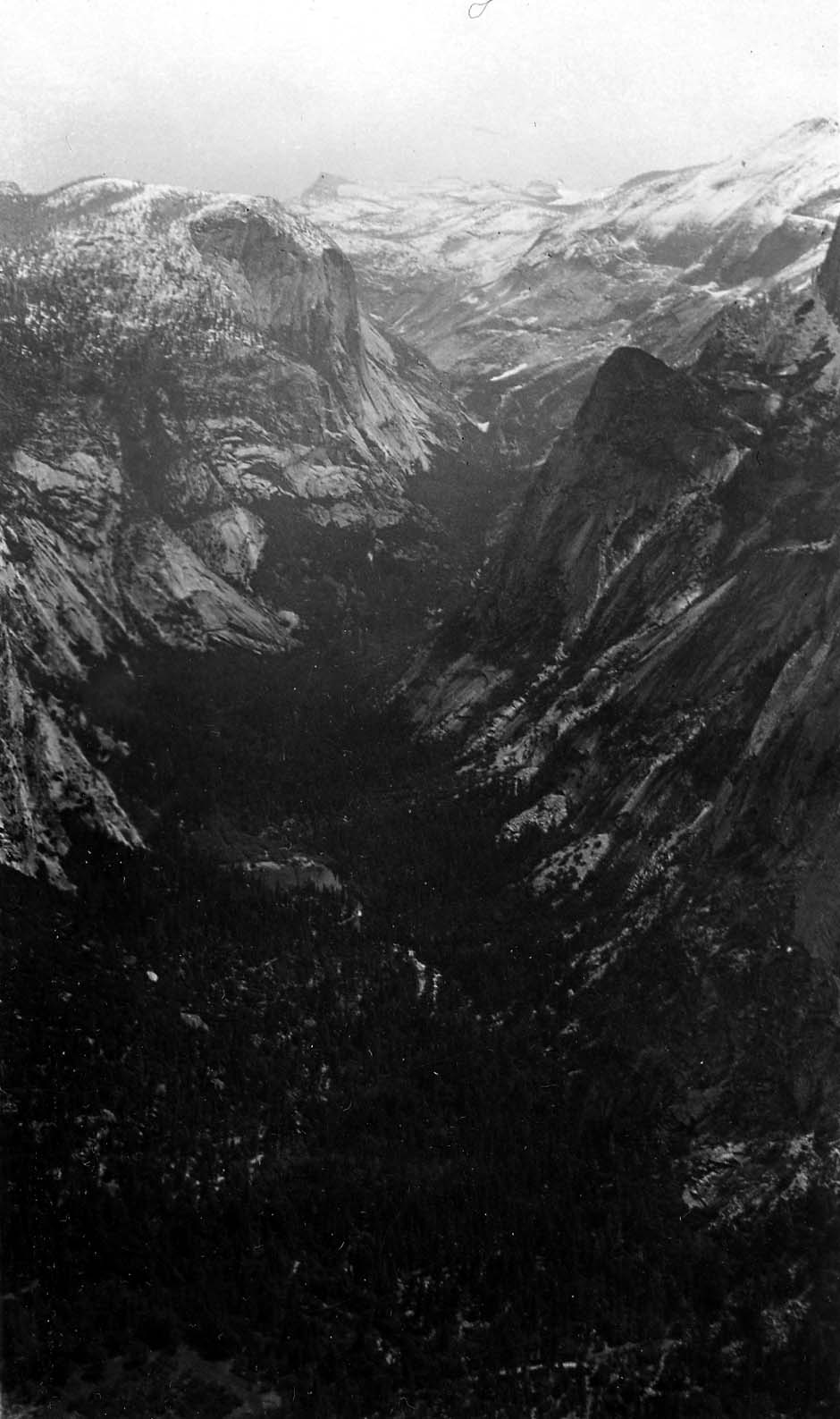 A dramatic high-angle view looking down into the deep, shadowed chasm of Tenaya Canyon flanked by sheer snow-dusted granite walls.