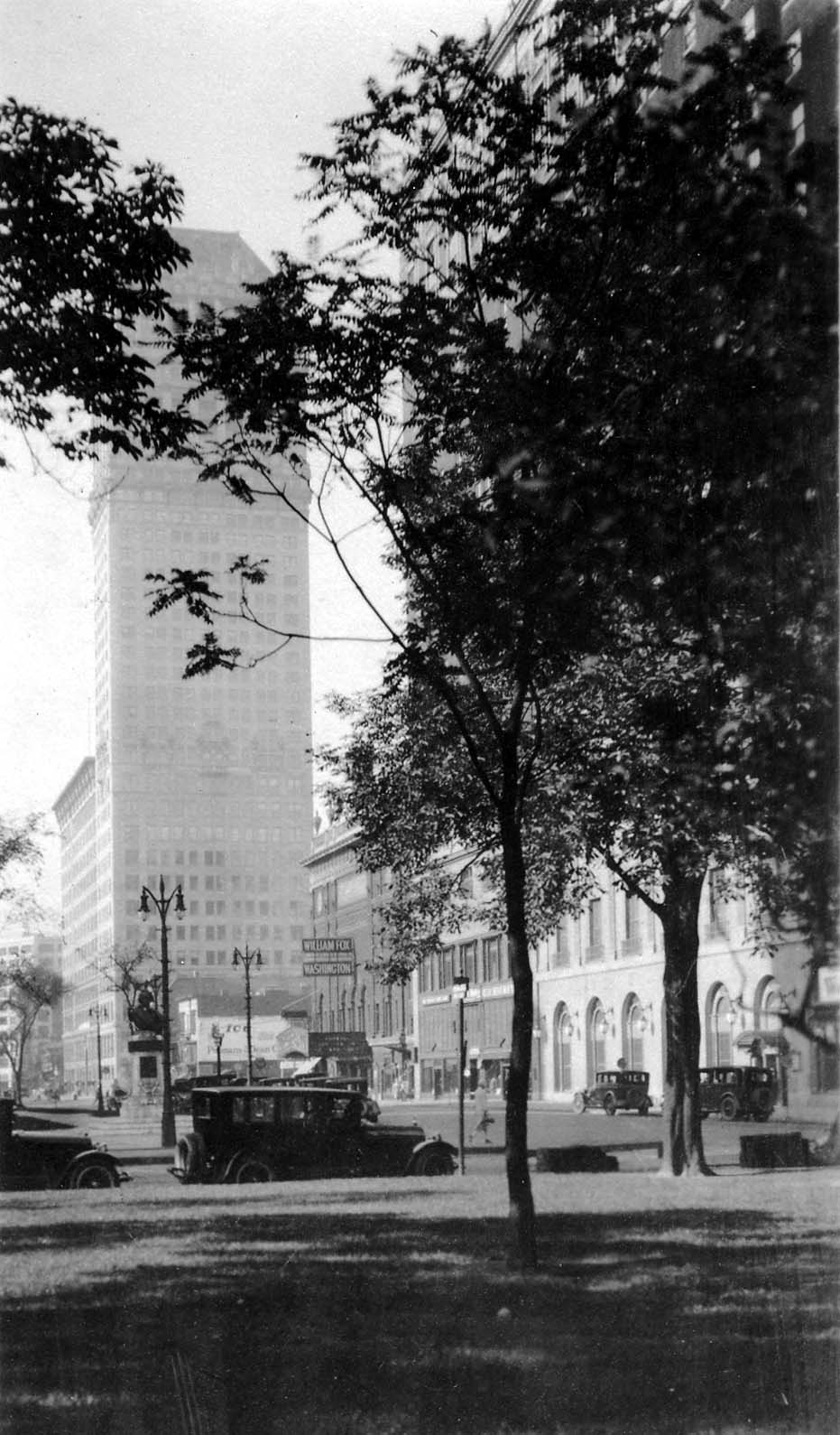 Looking down Washington Boulevard from Grand Circus Park showing vintage automobiles, the William Fox Washington Theatre, and skyscrapers.