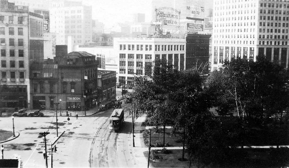 A high-angle view looking down at a Detroit streetcar turning onto Woodward Avenue outside Grand Circus Park near the Truscon building.