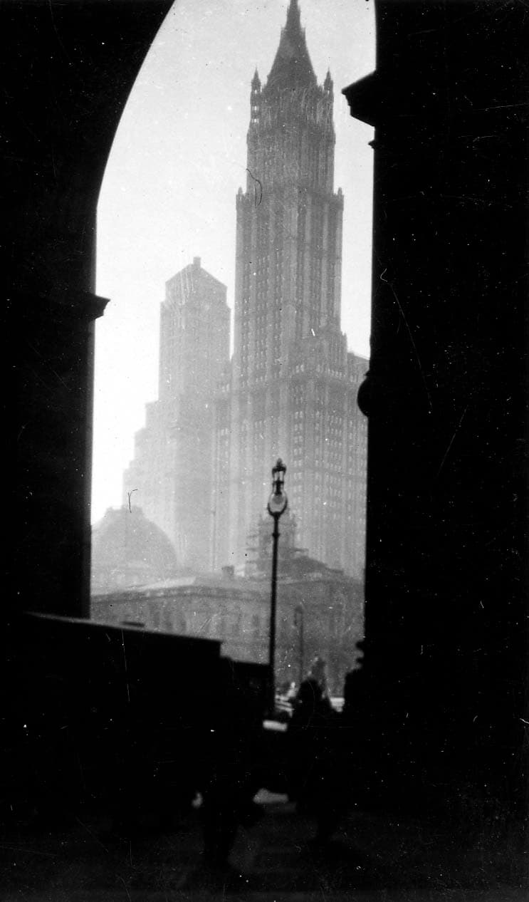 The iconic Gothic spire of the Woolworth Building framed dramatically through the grand classical arch of the Manhattan Municipal Building.