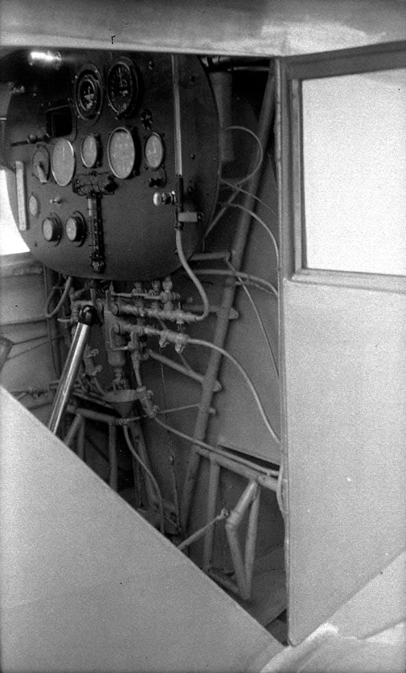 Interior view through the open cockpit door showing the instrument board and complex lower fuel plumbing manifold.