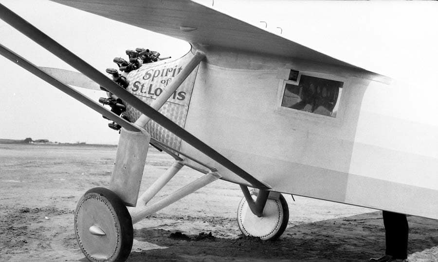 Close-up of the Spirit of St. Louis forward fuselage showing engine cowl, periscope housing, and a person standing behind the frame.