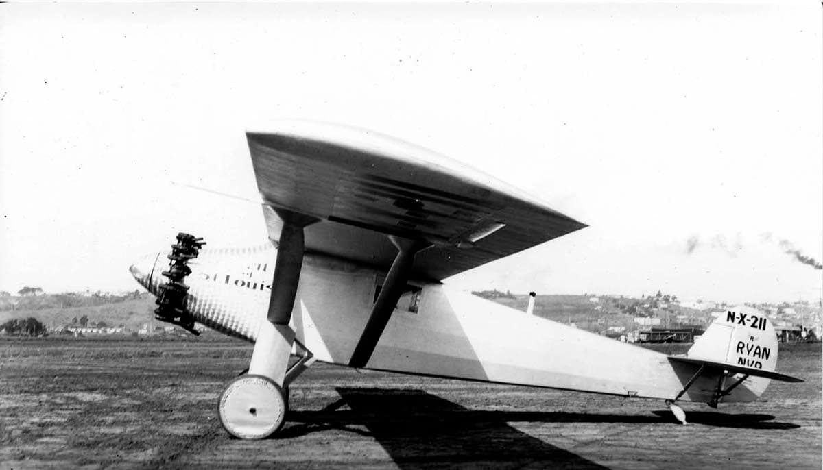 Archival left profile photograph of the Spirit of St. Louis on Dutch Flats with empennage markings and distant smoke.
